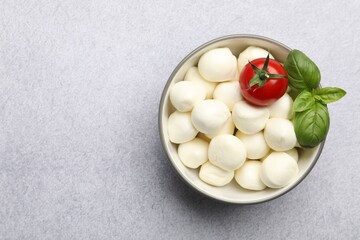 Tasty mozzarella cheese balls, tomato and basil on light grey table, top view. Space for text
