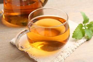 Aromatic lemon balm tea in glass cup, teapot and fresh leaves on wooden table, closeup