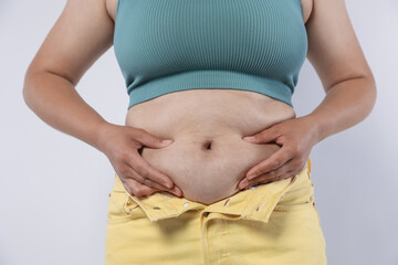 Woman with excessive belly fat on light background, closeup. Overweight problem