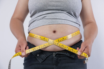 Overweight woman measuring her belly with tape on light background, closeup