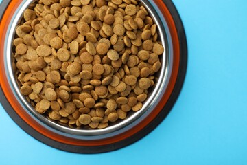 Dry pet food in feeding bowl on light blue background, top view