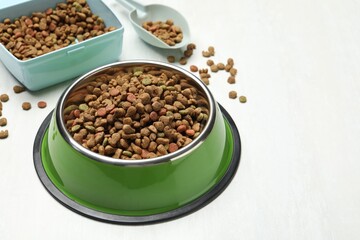 Dry pet food in feeding bowl, container and scoop on light background, closeup
