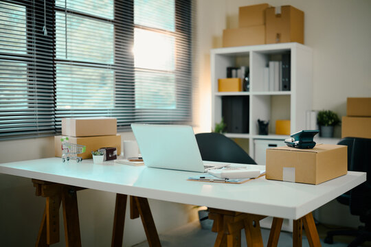 E-commerce home office with laptop, shipping parcels, and packaging tools on a white desk