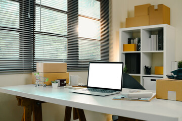 E-commerce home office with laptop, shipping parcels, and packaging tools on a white desk