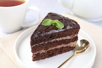 Piece of delicious chocolate cake with mint and spoon on light table, closeup