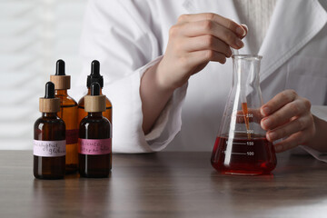 Professional perfumer developing luxury perfume at wooden table in laboratory, closeup