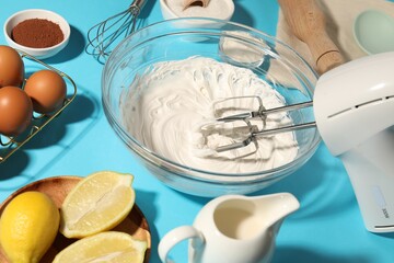 Hand mixer with whipped cream, eggs and other products on light blue table, closeup