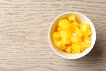 Pieces of fresh yellow bell pepper in bowl on wooden table, top view. Space for text