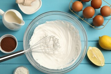 Whisk with whipped cream, eggs and other products on light blue wooden table, flat lay