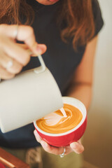 A close-up shot of a hand pouring milk art into a red cup of coffee.