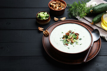 Tasty cucumber soup with dill and walnuts served on black wooden table. Space for text