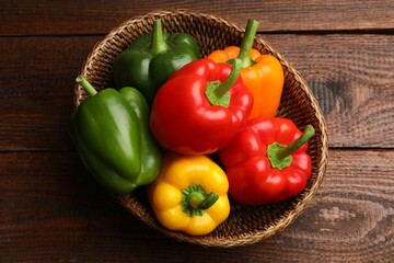 Fresh colorful bell peppers in wicker basket on wooden table, top view