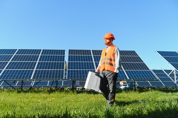 Worker walking in solar panel farm carrying equipment