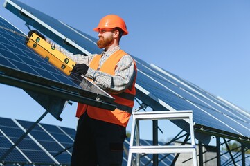 Worker installing solar panels in solar power station using level tool