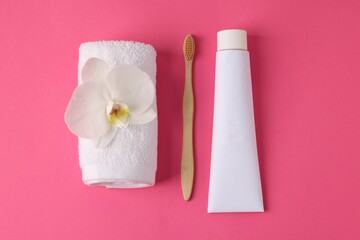 Toothbrush, toothpaste, towel and orchid flower on pink background, flat lay