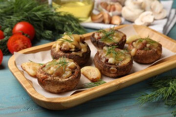Delicious stuffed mushrooms with melted cheese, garlic and dill on light blue wooden table, closeup