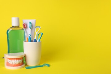 Different oral care products and dental model on yellow background, space for text