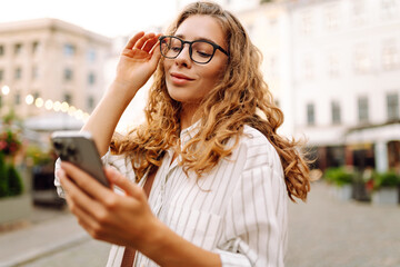 Portrait of a beautiful woman in glasses holding a phone on a sunset street. Beautiful woman...
