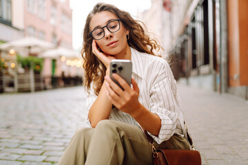 Portrait of a beautiful woman in glasses holding a phone on a sunset street. Beautiful woman...