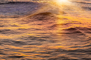 Water surface with waves lightened by the sun at sunset, sea background