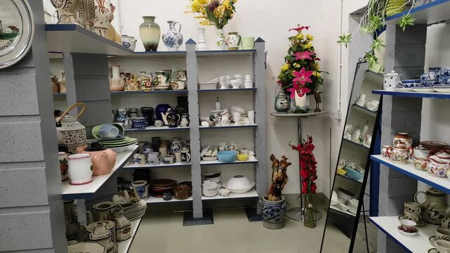 Inside a thrift store in Germany. Dinner plates and other ceramics on shelves. Panning shot.