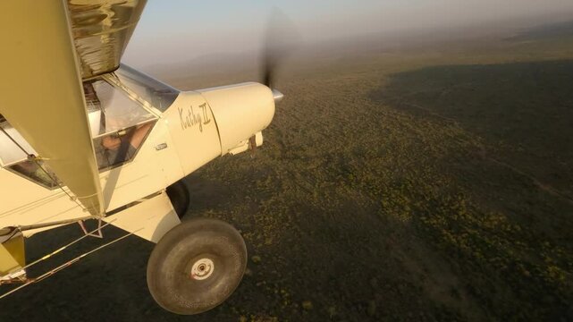 Hyperlapse of wide from light plane flying over savannah with aerial of vegetative landscape with shadow casting at sunset in Kenya 