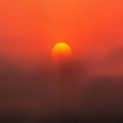 Sunset with glowing orange sun emerging from colorful haze, nature concept
