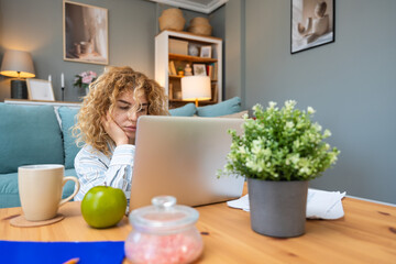 Young woman struggling with focus while working on laptop on floor, surrounded by printed analytic,...