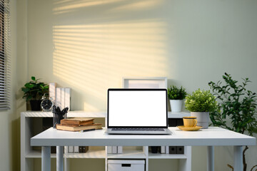 Minimalist desk with laptop, potted plants, alarm clock, and warm toned lighting
