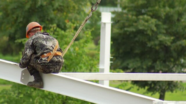 A worker fitter in a protective suit and helmet assembles a metal structure at a construction site in summer, industry. Copy space for text