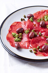 Slices of beef carpaccio with olives and capers. Close up.	