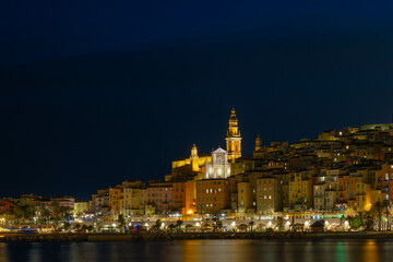 Obraz premium Night panorama of Menton in France. The lights of the night city are reflected on the calm sea surface.