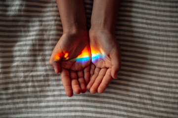 Two hands with palms facing upwards with rainbow-colored light reflection.