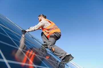 Technician installing solar panels on roof with blue sky background