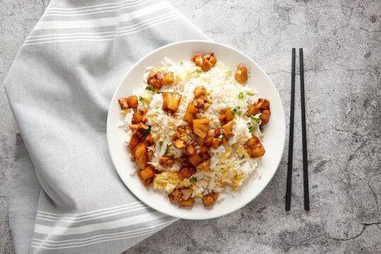 Fried rice topped with pineapple chicken served in a white plate.