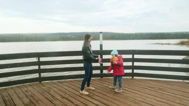 Mother and daughter at the pier near the water having fun. Mom with little girl playing a ball