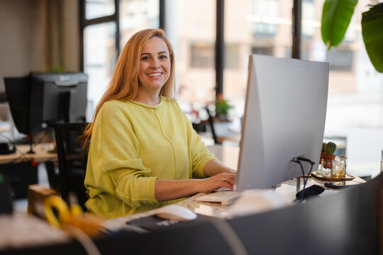 Smiling woman working on desktop computer in modern office