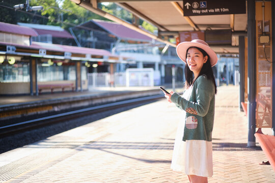 Young Asian woman standing on the train station platform with pink hat