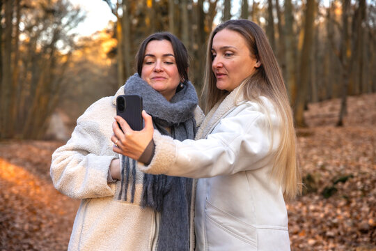 Two friends taking a selfie on their phone in the forest. Friends in nature.