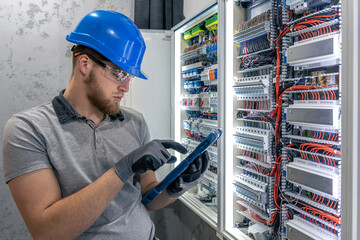 Electrician inspects switchboard. Tablet in hand. Digital and manual workflow.
