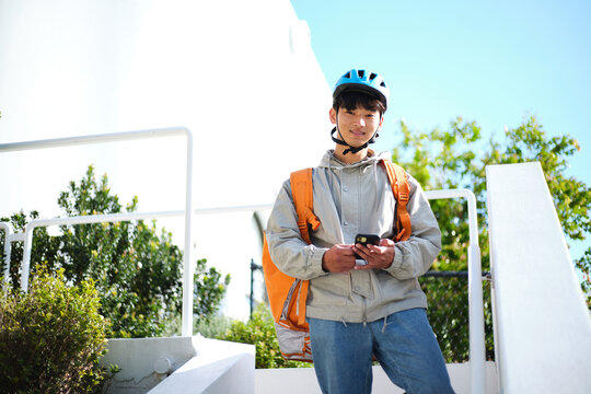 Young Asian delivery guy standing along the stairs while holding his phone