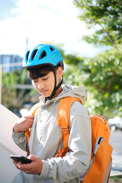 Young Asian delivery guy looking on his phone outdoors.