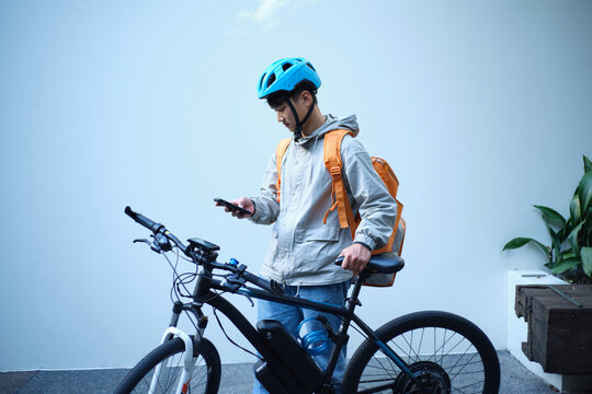 Young Asian delivery guy standing beside his bicycle