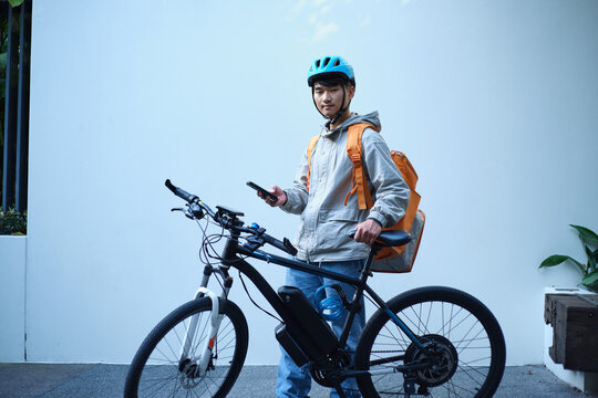 Young Asian delivery guy standing beside his bicycle.