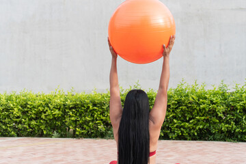 Latin woman doing pilates with orange fitness ball outdoors