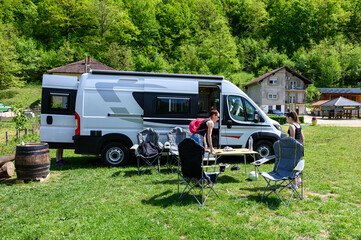 Family camping with a campervan in a campsite in Bosnia near Una River. Family relaxing with camper van, chairs and table on vacation.