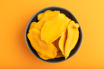 Dried Mango in blue ceramic bowl on orange pastel paper. Top view, copy space