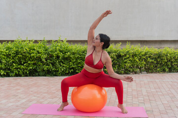 Plus-size woman doing pilates on fitness ball outdoors