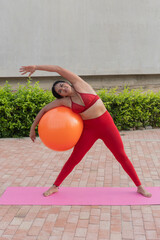 Young woman doing pilates exercises with swiss ball outdoors