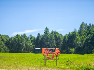 A lifebuoy and life jacket are hanging on a wooden fence the backdrop of a forest.